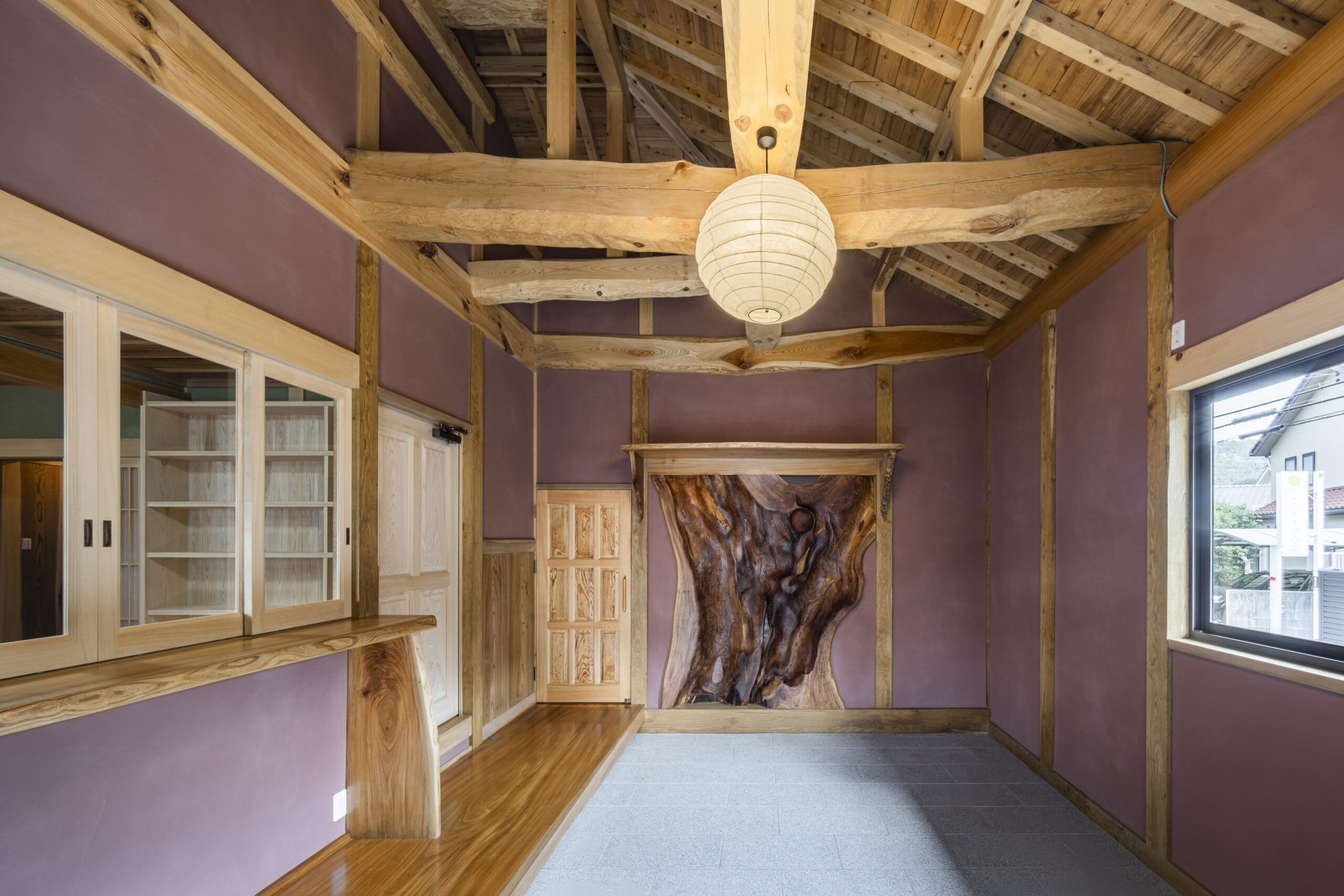 天井に木の梁が渡り、紫がかった壁の玄関土間に、ケヤキの株を用いた木の板が正面に配され、照明が吊られた空間